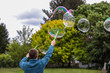 © Dmitry - A man in blue fleece jacket making giant soap bubbles with two green wands and a rope