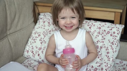 close up of little cute baby girl sit on bed waking up in morning, holds in hands bottle of milk, sm
