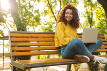Happy Young Beautiful Curly Student Girl Sitting Outdoors In Nature Park Using Laptop Computer.