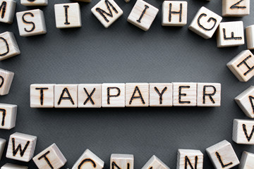 Fototapete - the word taxpayer wooden cubes with burnt letters, debts, gray background top view, scattered cubes around random letters