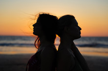Close Up Silhouette Of Womens Couple In Romantic Scene Of Sunset Over The Sea. Beautiful Female Young Lesbian Couple In Love.