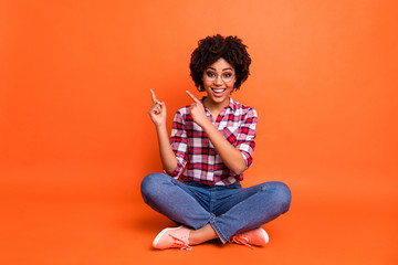 Poster - Portrait of nice attractive beautiful lady sit floor indicate fingers empty space shopping wear specs casual jeans denim checkered plaid shirt isolated orange background