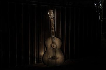 Wall Mural - An wooden acoustic guitar is against a grunge textured wall. The room is dark with a spotlight for your copyspace.