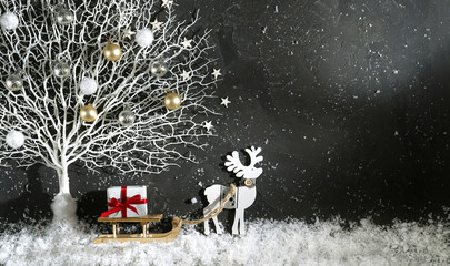 Wall Mural - Festive Christmas background template - .bright black scene decoration color with white tree in snow and toy reindeer with wooden sleigh with box gift with red ribbon, copy space, top view.