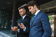 Image of confident businessmen partners standing outside office center and holding cellphones together during working meeting