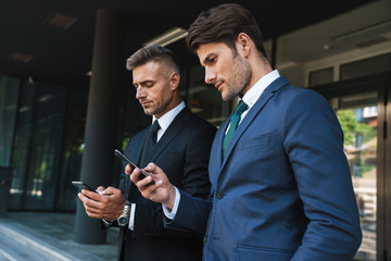 Wall Mural - image of confident businessmen partners standing outside office center and holding cellphones togeth