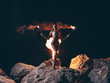Young sexy woman with a gorgeous slim body in bikini is staying (posing) at the dark night on the rock with the lit by fire torches in her hands. Black sky at the background