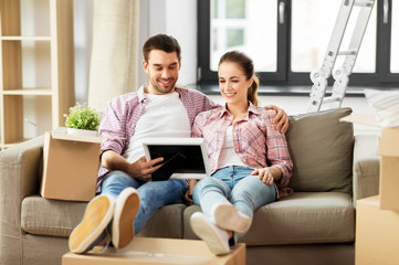 Wall Mural - moving, people, repair and real estate concept - happy couple with photo frame and cardboard boxes sitting on sofa at new home