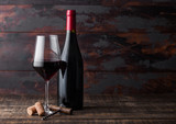 Elegant glass and bottle of red wine with corks and corkscrew on dark wooden background. Natural Light