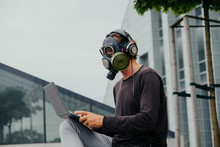 A Man In A Gas Mask In The City With A Laptop Phone And Headphones