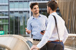 © Drobot Dean - Cheerful happy young two friends colleagues business men standing near business center talking with each other using mobile phone.