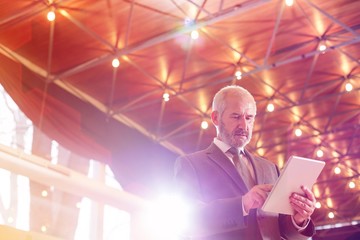 Low angle view of confident senior businessman using digital tablet while standing against illuminated roof