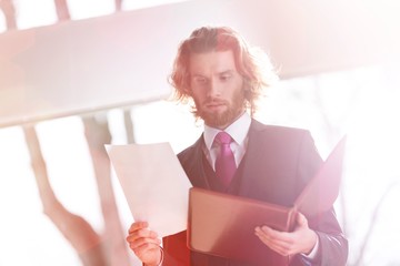 Wall Mural - Confident young businessman reading document while standing against window at office