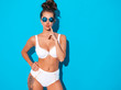 © halayalex - Young beautiful sexy woman with ghoul hairstyle. Trendy girl in casual summer white swimsuit in sunglasses.Hot model isolated on blue.Makes duck face