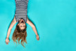 Laughing girl laying on blue backdrop up side down. Smiling, happy child. Childhood memories. Having fun. Joyful kid having great time in striped dress top view. Childlike glee. Simple wallpaper