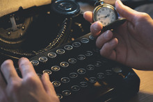 A Writer Is Typing A Book And Looking On A Pocket Watch Is His Hand And Is Sitting By His Table.