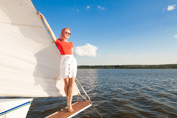 Model in a red blouse, white skirt, glasses, a red scarf on his head, standing on a white yacht, overlooking the sea and the blue sky, with a place for the inscription. The concept of luxury.