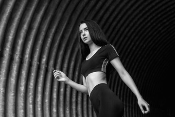 Sports woman running in fashion sportswear on tunnel urban gray background. Fitness model working out outdoor. Young beautiful slim brunette girl in trendy leggings and top. Black and white.