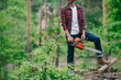 © LIGHTFIELD STUDIOS - partial view of lumberman in plaid shirt and denim jeans standing with chainsaw in forest