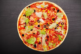 Fototapeta  - Tasty pizza with various flavored ingredients on a dark background