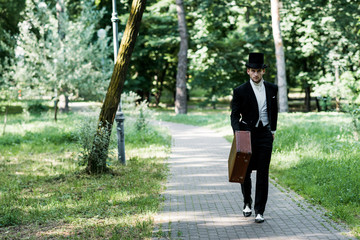 Wall Mural - handsome victorian man in hat holding baggage and walking outside