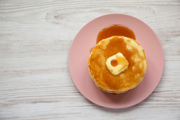 Wall Mural - Stack of homemade pancakes with butter and maple syrup on a pink plate on a white wooden background, top view. Overhead, from above, flat lay. Copy space.