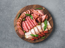 Antipasto Set Platter Wooden Plate On Gray Stone. Cold Smoked Meat Plate With Sausage, Sliced Ham,prosciutto,bacon,olives,basil. Appetizer On Wooden Tray Cut Tree Sawed Imitation. Copy Space. Top View