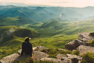 Travel man tourist sitting alone on the edge mountains over green valley adventure lifestyle extreme vacations green landscape Freedom