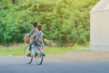 Back view of happiness two brothers wear military camouflage shirts ride bicycle at modern organic farmhouse