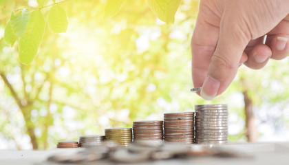 Businessman hand putting coins stack on table with blur nature bokeh background in park. Concept financial saving success growing investment.