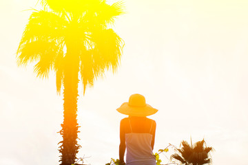 Silhouette of a girl in a hat and palm trees with a bright summer gradient on a bright blue background of summer sky. A concept is tropic, vacation and travel