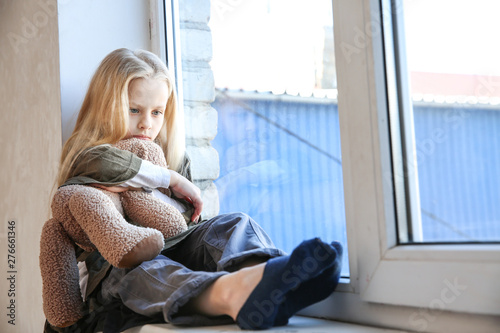 Fotomural Homeless little girl with teddy bear sitting on window sill