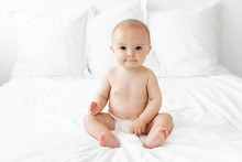 Baby In Diaper Sitting On White Bed
