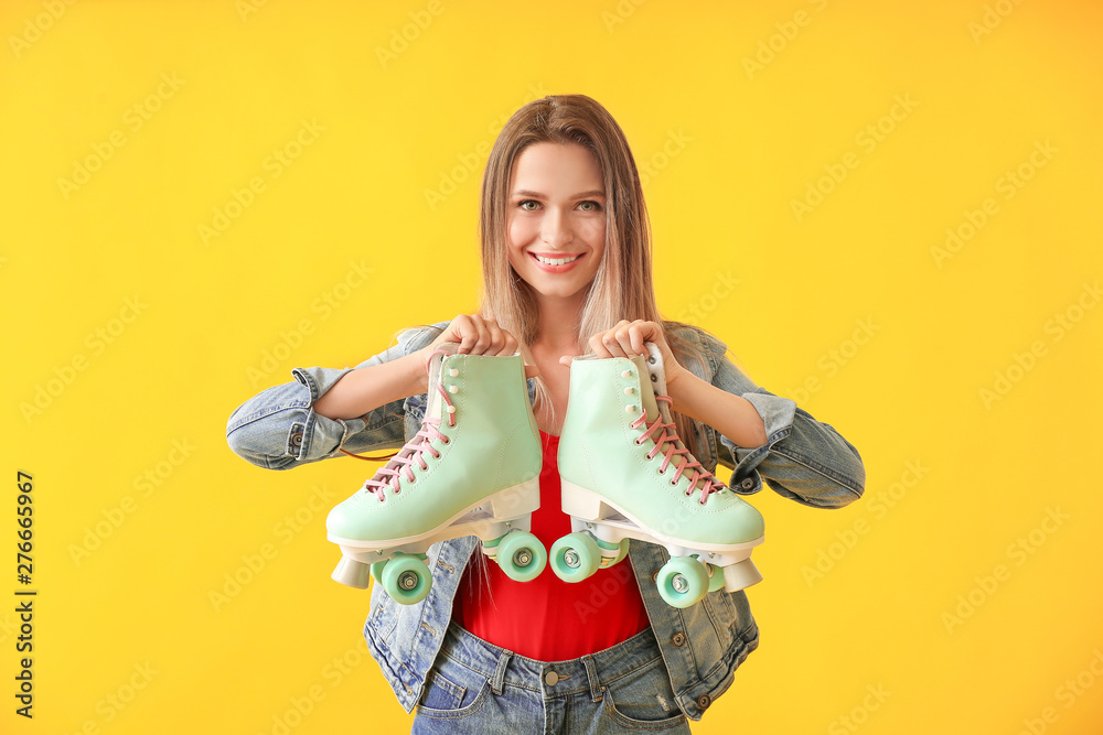 Beautiful young woman with roller skates on color background