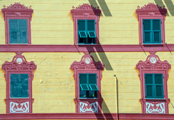 Canvas Print - Close-up of the multicolored façade of an old building in the historical centre of Rapallo with rows of green shutters and trompe l'oeil decorations in red and yellow colors, Genoa, Liguria, Italy 