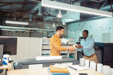 Canvas Print - Dark-skinned colleague giving roll of paper to writer