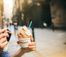Girl Is Eating Tasty Ice-cream In The Street. Woman's Hand Holding Plastic Spoon. Perfect Cold Summer Dessert. Food Photo. Relaxing On Holidays.