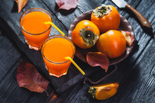A Glass Of Fresh Juice And Ripe Orange Persimmon Fruit And Persimmon Leaves In A Brown Plate On A Black Wooden Table. Fresh Fruits