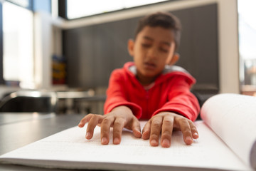 Blind schoolboy hands reading a braille book at desk in a classroom