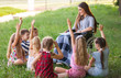 © Andrey - children hold a lesson with the teacher in the park on a green lawn.