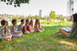 © Andrey - children hold a lesson with the teacher in the park on a green lawn.