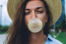 Young Attractive Woman In Hat Blowing Bubble Of Chewing Gum Outdoor