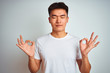 Young asian chinese man wearing t-shirt standing over isolated white background relaxed and smiling with eyes closed doing meditation gesture with fingers. Yoga concept.