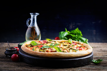 Wall Mural - Italian pizza with chicken, salami, zucchini, tomatoes and herbs on vintage wooden background.  Italian cuisine