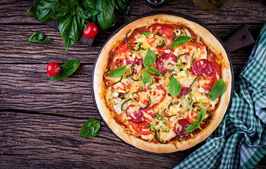 Wall Mural - Italian pizza with chicken, salami, zucchini, tomatoes and herbs on vintage wooden background. Top view. Italian cuisine