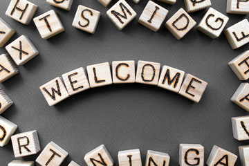 Fototapete - the word welcome wooden cubes with burnt letters, hospitality, gray background top view, scattered cubes around random letters