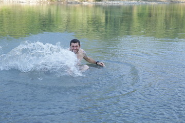 active young happy man makes a splash in the water of a clear mountain river or lake