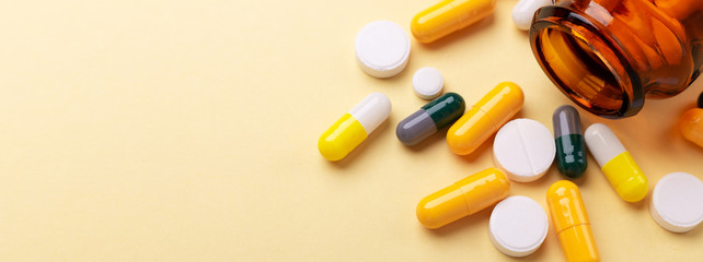 multicolor tablets and pills capsules from glass bottle on yellow background health care close-up ho