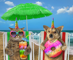 Wall Mural - The dog unicorn with a donut and the cat in sunglasses with a glass of colored cocktail are sitting under the green straw umbrella on a beach chairs on the sea shore.