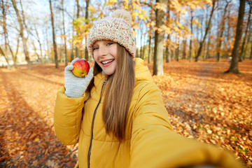 Poster - season and people concept - happy girl with apple taking selfie at autumn park